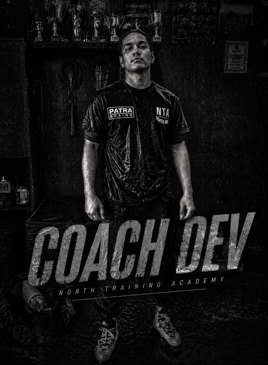 Coach Dev standing inside Patra Boxing beneath the gym's trophies.